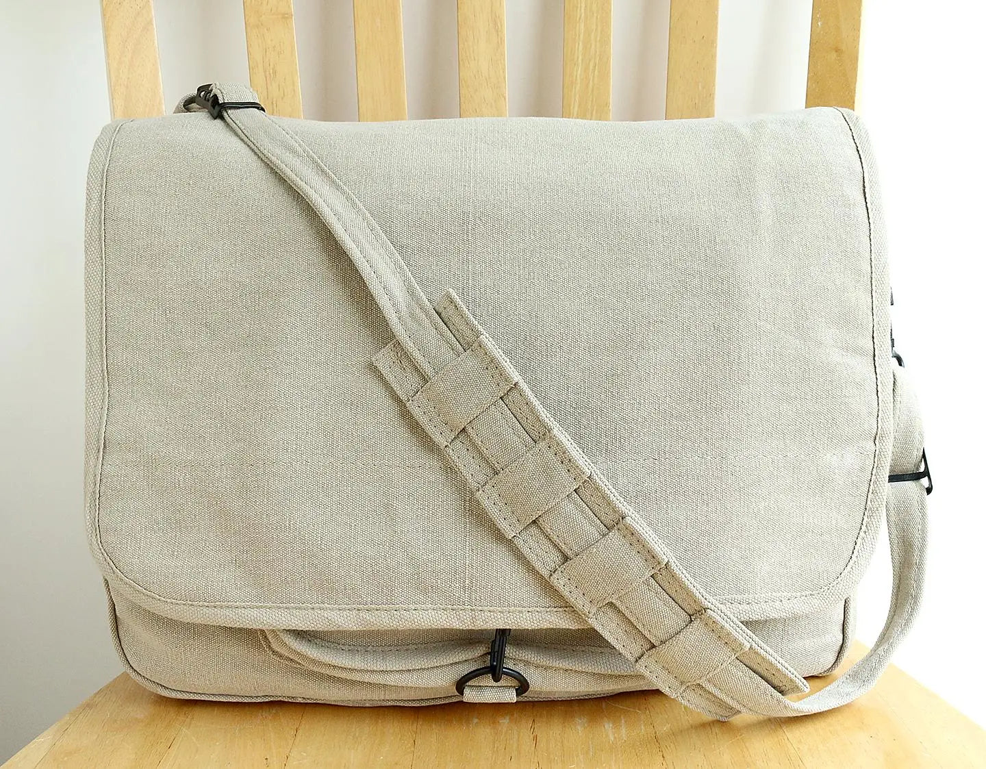 Beige canvas messenger bag with adjustable strap on a wooden chair