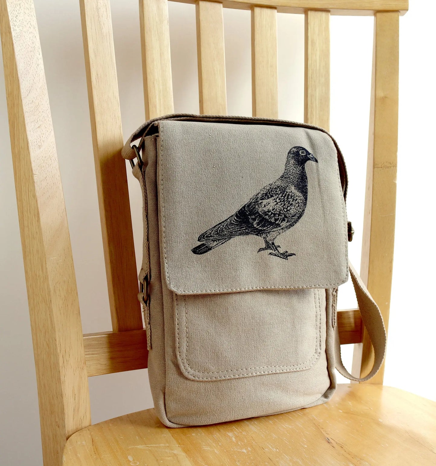 Beige canvas crossbody bag with black pigeon print, displayed on a wooden chair.