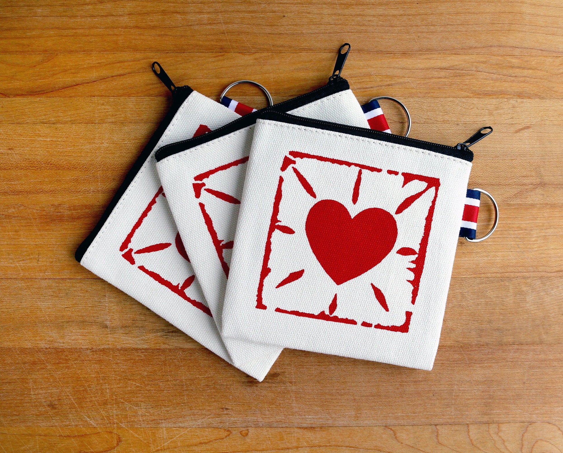 Canvas zippered pouches with red heart print and striped keyring on wood surface