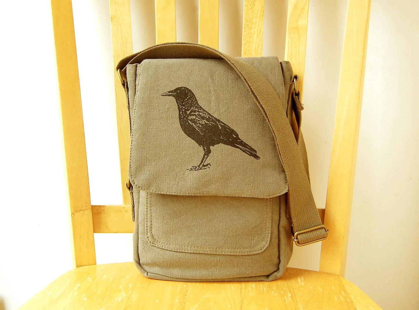 Hand printed canvas messenger bag with black bird design and adjustable strap on a chair