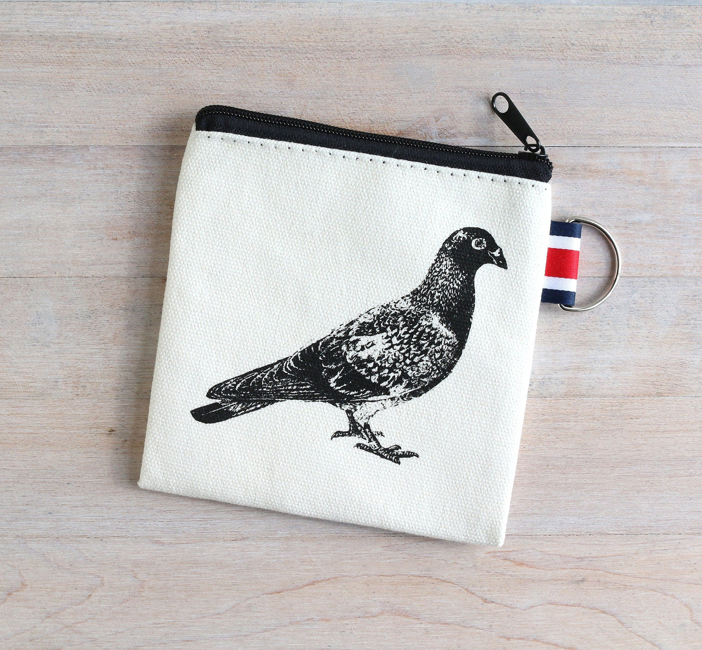 Canvas coin pouch with black pigeon print, striped keyring, and zipper closure