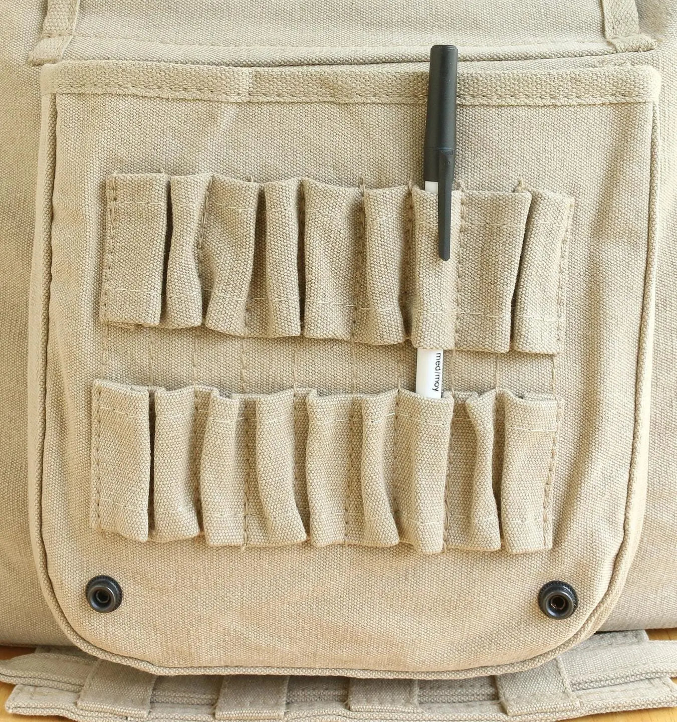 Beige canvas bag with multiple organizer pockets holding a pen, ideal for accessories