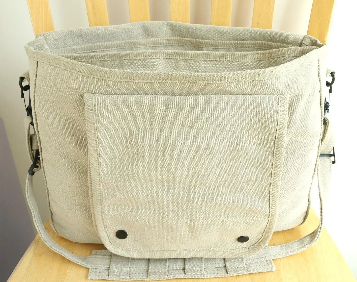 Beige canvas messenger bag with front pocket and adjustable strap on wooden chair