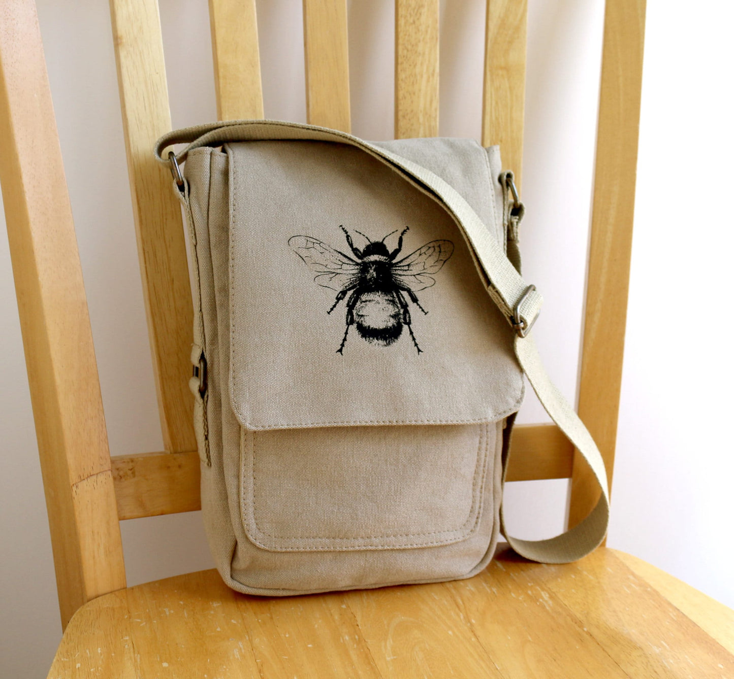 Hand printed crossbody bag with black bee illustration on beige canvas, displayed on a chair.