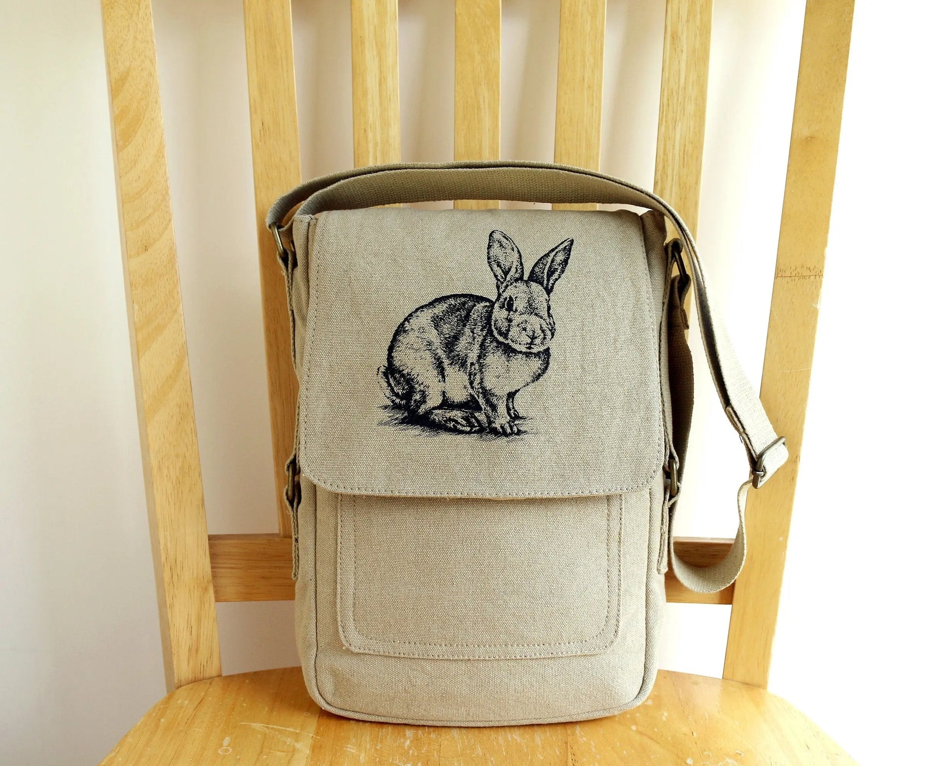 Linen crossbody bag with hand printed black rabbit design on flap, displayed on wooden chair.