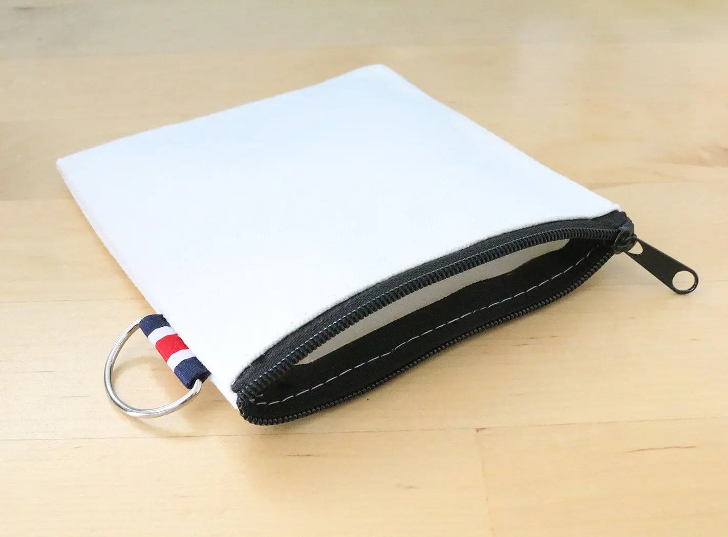 White zippered canvas pouch with black zipper and striped fabric key ring tab on wood surface
