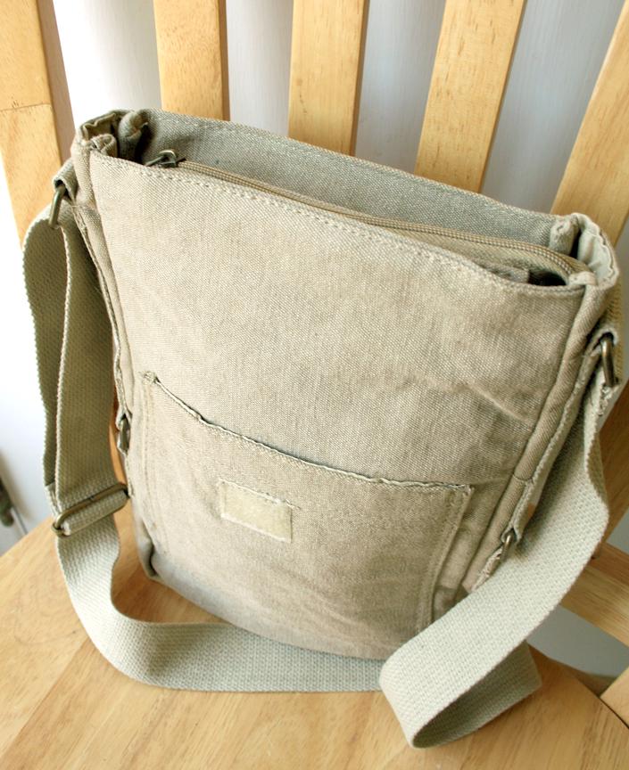Beige canvas crossbody bag with front pocket and adjustable strap on wooden chair
